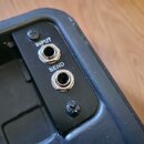Detailní pohled na černý panel s dvěma kovovými konektory typu jack. Nad horním konektorem je bílý nápis INPUT a nad spodním nápis SEND. Panel je při…