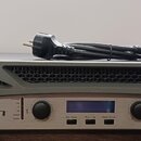 Šedý výkonový zesilovač s kovovým předním panelem stříbrné barvy. Na panelu je vlevo logo a nápis CROWN a vpravo označení 4002 XTi SERIES. Zařízení m…