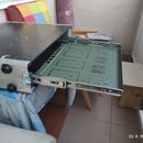 Stříbrný kovový rack s vysunutým šuplíkem. Vnitřek šuplíku je vyložen zelenou deskou s vyfrézovanými drážkami a otvory. Povrch horní desky racku je č…