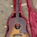 Akustická kytara s korpusem v barevném přechodu od žluté k tmavě hnědé (sunburst) a tmavým hmatníkem. Na hlavě nástroje je bílý nápis Gibson. Kytara…