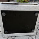Fotografie zachycuje spodní stranu černého transportního kufru s hliníkovým rámem a kovovými rohy. Na spodní černé ploše jsou umístěny čtyři kulaté g…