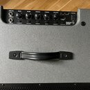 Šedý kytarový kombozesilovač s černým ovládacím panelem a plastovou rukojetí. Na panelu jsou nápisy INPUTS, GAIN, BASS, MIDDLE, TREBLE, VOLUME a POWE…