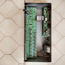 Fotografie zachycuje vnitřek elektronického zařízení v černém kovovém šasi. Uvnitř jsou umístěny dvě zelené základní desky s osazenými součástkami, k…