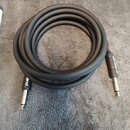 Černý instrumentální kabel sletovaný do kruhu. Na obou konech jsou kovové jack konektory a na černých plastových krytkách je bílý nápis "land". Povrc…