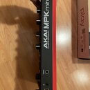 Fotografie zachycuje zadní stranu černého MIDI kontroléru s červeným bočním rámem. Na přístroji jsou nápisy AKAI PROFESSIONAL MPK mini play a čtyři č…