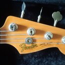 Detail hlavy elektrické basy v přírodní dřevěné barvě. Na hlavě je černé logo Fender a nápisy JAZZ BASS, MADE IN USA a ELECTRIC BASS. Nástroj má čtyř…