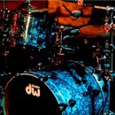 Modrá bicí souprava s mramorovým povrchem. Na předním rezonančnímstěně basového bubnu je bílé logo „drums dw“. Souprava obsahuje několik bubnů a čine…
