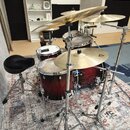 Fotografie zobrazuje bicí sadu v tmavě červeném přechodovém odstínu s chromovaným hardwarem. Sada obsahuje snare drum, dva tom-tomy a činely umístěné…