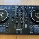Černý DJ kontrolér s dvěma jog-koly a centrálním mixážním sekcí. Na přístroji je bílý nápis Pioneer DJ a modelové označení DDJ-400 s doplňkem rekordb…