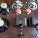 Fotografie zobrazuje sadu reproduktorů a dvou černých plastových modulů s kovovými držáky. Na dvou větších černých reproduktorech je na magnetu nápis…