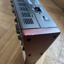 Fotografie zachycuje zadní část černého elektronického zařízení s ventilační mřížkou. Je vidět napájecí konektor a vypínač s nápisem POWER a symboly…