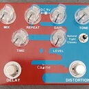 Červený efekt pedál s modrými prvky a průhlednými oválnými knoflíky. Na zařízení jsou nápisy MIX, REPEAT, GAIN, TONE, TIME, LEVEL, OUTPUT, INPUT a v…