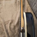 Detailní pohled na hranu hmatníku a korpus kytary. Hmatník je tmavý s viditelnými pražci, krk je vyroben ze světlého dřeva a korpus je černý s bílým…