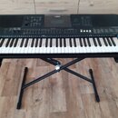 Černý digitální klavír umístěný na černém X-stojanu. Na horní části je uprostřed bílé logo YAMAHA a vpravo nápis PSR-E453. Nástroj má bílé a černé kl…