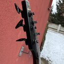 Fotografie zachycuje hlavu černé elektrické kytary s třemi ladicími kolíky na jedné straně. Na čele hlavy je bílé logo znázorněné jako stylizované pí…