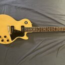 Elektrická kytara s žlutým povrchem korpusu a hnědým hmatníkem. Na hlavě je viditelný nápis "Les Paul". Nástroj má dva snímače, čtyři černé ovládací…