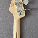Zadní strana hlavy a krku světlé dřevěné basové kytary. Na hlavě jsou čtyři kovové ladičky a nápisy „Fender“, „Custom Offset“, „Made in USA“ a sériov…