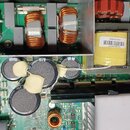 Fotografie zachycuje vnitřní elektronické součásti zařízení na zelené základní desce. Jsou zde vidět měděné cívky, kondenzátory a žlutý transformátor…