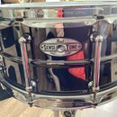Černý snare drum s chromovaným hardwarem. Na korpusu je oválný štítek s nápisy „Pearl“, „SENSITONE“ a menším textem „MADE IN TAIWAN“. Na horním i dol…