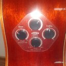 Detail ovládacího panelu akustické kytary s červeně hnědým povrchem. Panel obsahuje čtyři černé otočné knoflíky a nápisy: Bass, Treble, SRT Blend, Pu…