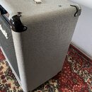 Šedý kytarový kombozesilovač potažený texturovaným vinylen. Na přední straně je vidět část bílého nápisu "Marshall" a černá textilní mřížka. Rohy jso…
