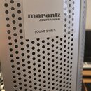 Detail stříbrného kovového povrchu s perforací v podobě malých otvorů. Na povrchu je přilepený bílý čtvercový štítek s nápisy marantz, PROFESSIONAL a…