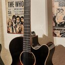 Akustická kytara s cutawayem v tmavém sunburst provedení. Na hlavě hmatníku je viditelný nápis "langleed". Nástroj visí na nástěnném držáku v místnos…