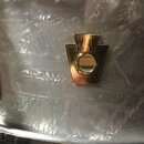 Detailní záběr na stříbrný, texturovaný povrch bubnu s kovovým zlatým štítkem. Na štítku je nápis DRUMS a v dolní části text LUDWIG DRUM CO. CHICAGO…