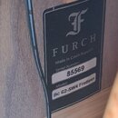 Detailní záběr na černý štítek s bílým textem přilepený k dřevěnému povrchu. Štítek obsahuje logo ve tvaru stylizovaného písmene F a nápis FURCH Made…