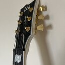 Detail hlavy elektrické kytary v černé barvě s bílým lemováním. Na hlavě je bílé logo Ltd a nápis Deluxe. Ladicí kolíky jsou zlaté barvy. Hmatník je…