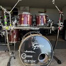 Vícedílná bicí souprava v červeném metalizovaném provedení s kovovým hardwarem. Na basovém bubnu je vidět logo Gretsch a nápisy Anatolian, AQUARIAN D…