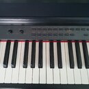 Černý digitální klavír s bílými a černými klávesami. Na ovládacím panelu jsou tlačítka s nápisy ACCOMP, RHYTHM, BASS, CHORD, LOWER, UPPER aTlačítka s…