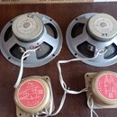 Dva šedé reproduktory s magnetem, na kterých je bílý štítek s nápisy „Goodmans of England“, „MADE IN ENGLAND“ a „GOODMANS LOUDSPEAKER UNIT“. Pod nimi…