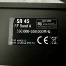 Fotografie detailně zachycuje černý štítek s bílým textem na černém povrchu zařízení. Na štítku jsou nápisy SR 45, RF Band A a frekvenční rozsah 530.…