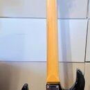 Fotografie znázorňuje zadní stranu elektrické kytary s trupem v černo-oranžovém přechodovém lakování (sunburst) a krčkem v žluté barvě. Na zadní stra…