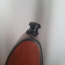 Detailní pohled na spodní část hřdelníku akustické kytary z reddish-brown dřeva s černým lemováním. Na koncnu je připevněn černý plastový nebo kovový…