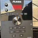 Černý elektronický bicí modul značky ALESIS s nápisem CRIMSON II v levém dolním rohu a ADVANCED DRUM MODULE v pravém dolním rohu. Zařízení má digitál…