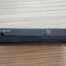 Černý elektronický přístroj s kovovým konektorem na levém okraji. Na šasi je bílý nápis Ω/LINE OUT u audio konektoru a nápis HOLD nad posuvným přepín…