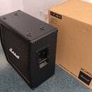Černý kytarový reproduktor s logem Marshall na přední síťce. Vedle něj stojí hnědý kartonový obal s nápisy MG412A GOLD, Marshall a MARSHALLAMPS.COM |…