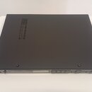 Černý elektronický přístroj s matným povrchem a ventilační mřížkou v horní části. Na předním panelu je viditelné logo SHURE a několik ovládacích tlač…