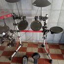 Elektronická bicí souprava s černými pady a činely na stříbrném kovovém rámu s červenými prvky. Na modulu je viditelný nápis YAMAHA a DTX. Na povrchu…