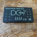 Černý napájecí zdroj pro efektové pedály s nápisy „Future Power Generation“ a „DC 7“. Na horní části je bílé logo „CIOKS“ a označení „POWER SUPPLY“.…