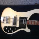 Bílá elektrická basová kytara v černém kufru. Nástroj má černý pickguard, jeden snímač s kovovým krytem a čtyři ovládací knoflíky. Na těle nejsou žád…