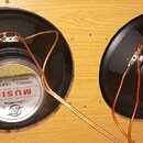 Dva černé kruhové reproduktory s kovovými magnety zamontované v dřevěné desce. Na zadní straně magnetů je bílo-červený štítek s nápisy MUSIC, SoundKi…