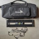 Černá transportní taška s nápisem Palmer pedalbay 4plus. Pod ní je černý kovový pedalboard s nápisem PEDALPOWER a LEWITZ. V dolní části jsou rozložen…