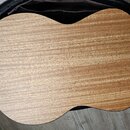 Fotografie zachycuje zadní část akustického nástroje, pravděpodobně kytary nebo ukulele, s povrchem z dřeva s viditnou masivní strukturou žil. Nástro…