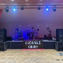 Fotografie zachycuje hudební stage s kompletním ozvučením a nástroji. V popředí jsou dva páry černých reproduktorů značky Bettsound, pod nimi je bann…