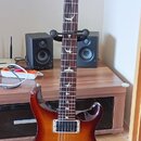 Elektrická kytara s trupem v červenohnědém sunburst provedení a tmavým hnedým hmatníkem. Na hlavě je zlaté logo Aria a svislý nápis Custom. Hmatník o…