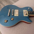 Modře lakovaná elektrická kytara s tmelemi v krémové barvě a dvěma humbuckery. Na těle jsou umístěny dva zlaté ovládací knofíky a jeden bílý přepínač…