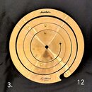 Zlatavý mosazný spirálový činelec s otvorem uprostřed. V horní části je nápis „Anatollian“ a v dolní části text „JC Mellow 12" SPIRAL“. Povrch vykazu…